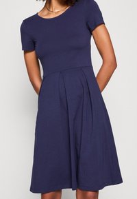 Abito blu navy a maniche corte con corpetto aderente e gonna svasata caratterizzata da pieghe. Realizzato in tessuto liscio con scollatura rotonda.