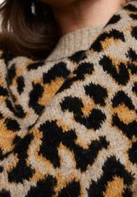 Pull en maille beige avec imprimé léopard noir et rouille. Présente un col côtelé et un tissu doux et texturé. Vue en gros plan du motif.