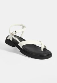 Witte leren sandalen met banden en een vlakke zwarte rubberen zool, met een ronde neus en een verstelbare enkelband. Getextureerde banden voegen detail toe.