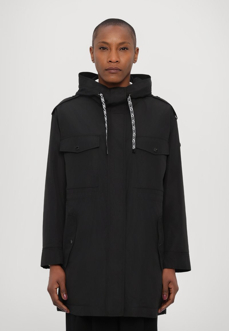 Parka noire avec capuche, dotée d'une fermeture éclair à l'avant, de deux poches poitrine et d'un cordon de serrage. Texture lisse et coupe légèrement oversize.