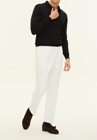 Marinblå långärmad polo skjorta i kombination med vita skräddarsydda byxor och bruna mocka loafers, med en texturerad finish och tofsdetaljer.