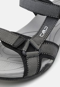 Sandales ajustables noires et grises avec des bandes textiles à motifs et une semelle grise rembourrée, dotée d'un lit de pied texturé et d'un matériel durable.