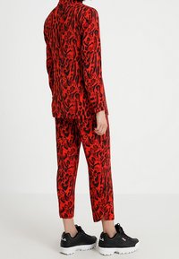 Punainen ja musta leopardikuvioinen puku, jossa on räätälöity takki ja kapealahkeiset housut, yhdistettynä mustiin tennareihin, joissa on valkoiset pohjat.