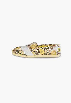 Los zapatos slip-on florales presentan una parte superior de tela en blanco y amarillo con un patrón de flores. La suela es de un amarillo claro, garantizando un diseño informal.