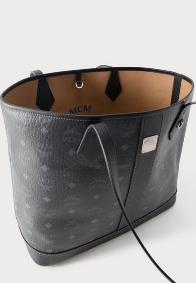 Sac fourre-tout en cuir noir texturé avec intérieur bleu portant le logo "MCM", deux bretelles pour épaules, plaque en métal et anneau porte-clés à l'intérieur.