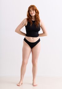 Débardeur noir sans manches et sous-vêtements taille haute assortis. Tissu lisse, conception ajustée et style minimaliste. Peau claire sans chaussures.