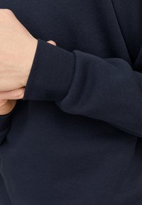 Détail d'un sweat-shirt bleu marine avec des poignets côtelés, mettant en avant un tissu doux et texturé avec une finition lisse et un minimum de couture.