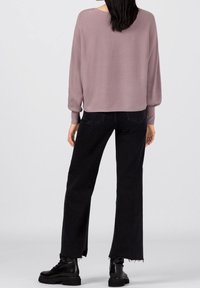 Pull en tissu mauve doux avec un col rond et des manches ballons, associé à un jean noir à jambes larges avec des ourlets effilochés et des bottes noires.