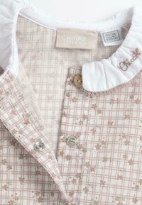 Ensemble pour bébé rose clair avec motif floral, col blanc et fermeture à boutons. Le matériau est doux, avec un design en quadrillage et une broderie délicate.