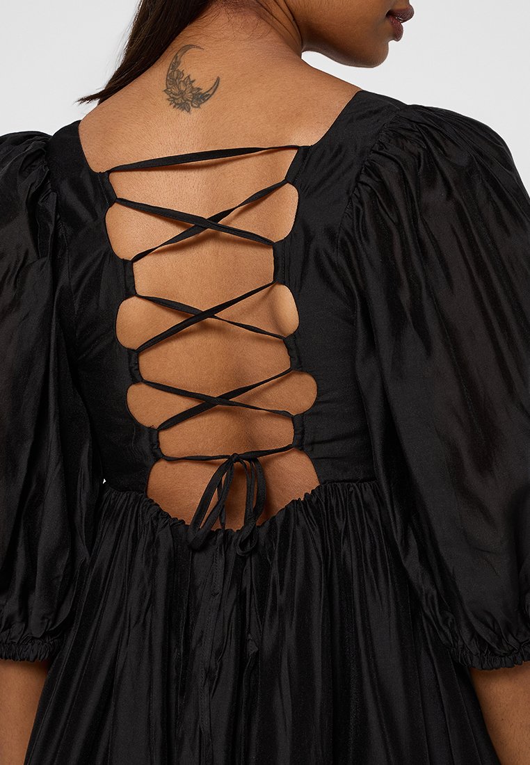 Robe en satin noir avec un dos en V profond et un détail de lacet entrecroisé, des manches bouffantes et une taille froncée pour une silhouette fluide.