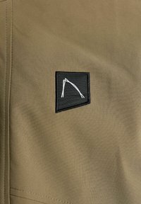 Toppa nera ricamata con design geometrico bianco su tessuto marrone con cuciture visibili, probabilmente materiale per abbigliamento.