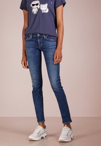 Jeans ajustados de color azul oscuro con un lavado desgastado, combinados con una camiseta gráfica en azul marino que presenta personajes de dibujos animados y zapatillas deportivas blancas.