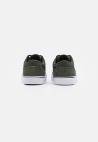 Grønne ruskind og kanvas sneakers med en hvid gummi sål, der har en sort stribe ved bunden og polstret krave for komfort.