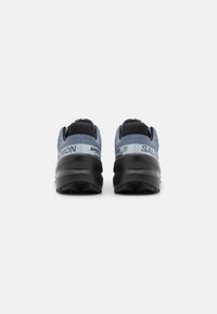 Baskets de trail de course bleues et noires avec une semelle robuste, un dessus en maille texturée et des détails de logo bien visibles au niveau du talon et sur le côté.