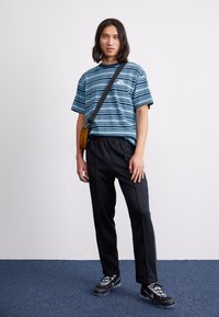 Stribet blå t-shirt med rund hals, sorte træningsbukser og sorte sneakers. Modellen bærer en brun crossbody taske. Enkel, afslappet outfit.
