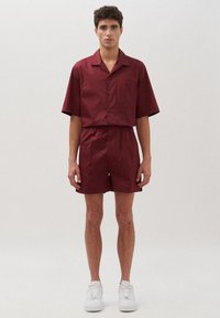 Set di camicia a manica corta bordeaux e pantaloni bermuda abbinati, realizzato in tessuto leggero, con colletto, tasca frontale e vita elastica.