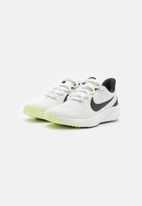 Baskets blanches en tissu texturé, avec le swoosh noir de Nike et une semelle extérieure verte. Présentent un orteil arrondi et un talon rembourré pour un meilleur soutien.