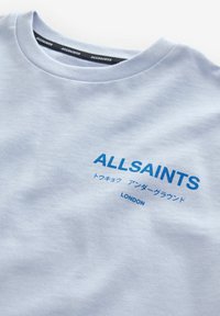 Artimas plano šviesiai mėlynos spalvos AllSaints marškinėlių su mėlynu tekstu, įskaitant japonų kalbos simbolius ir žodį "London" krūtinėje.