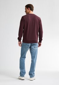Bordeaux sweatshirt met geribbelde manchetten en zoom, gecombineerd met lichtblauwe jeans en witte sneakers, met een eenvoudig, casual ontwerp.