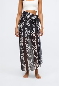 Gonna maxi nera trasparente con scritte bianche in corsivo, legata in vita, caratterizzata da una texture leggera e un design fluido.