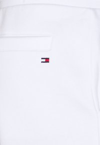 White cotton joggers featuring a small embroidered logo in red, white, and blue on the left side, with a rear pocket detail.