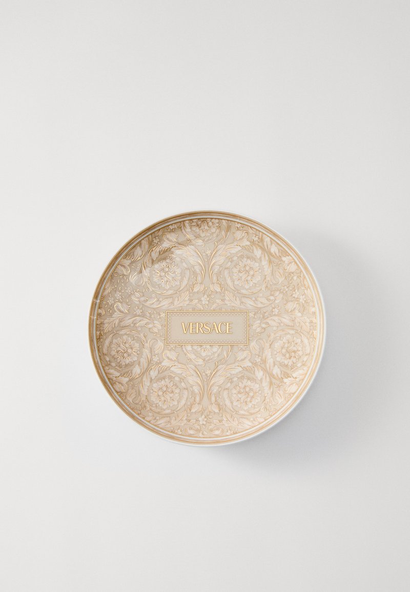 Okrągły ceramiczny talerz z detalicznym wzorem kwiatowym w delikatnym beżu, złotą obwódką i centralnym logo Versace umieszczonym w wyróżnionym prostokącie.