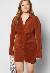 Vestido bodycon na cor rust, feito de um tecido texturizado, apresentando colarinho, mangas longas e fechamento frontal com botões com detalhes franzidos.