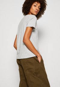 Gray cotton t-shirt with a crew neck and short sleeves, paired with olive-green cargo pants featuring large pockets and visible seams.