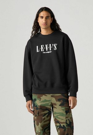Black Levi's sweatshirt with white logo text, featuring a crew neck and ribbed cuffs, paired with camouflaged cargo pants.