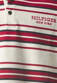 Czerwono-czarny i biały polo w paski z kołnierzykiem na dwa guziki oraz haftowanym logotypem "HILFIGER NEW YORK" na klatce piersiowej. Teksturowana tkanina.