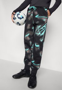 Sorte svedbukser med et turkist abstrakt design, elastisk talje med snor, sidelommer og ribbede manchetter. Spilleren holder en fodbold.