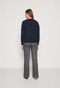 Pull marine avec un ourlet côtelé, associé à un pantalon évasé présentant un motif rayé vertical en gris et fils métalliques.