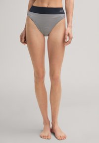 Vrouw die blootsvoets staat in hooggesneden marineblauwe en witte horizontaal gestreepte ondergoed met een marineblauwe tailleband en het JOOP! logo.