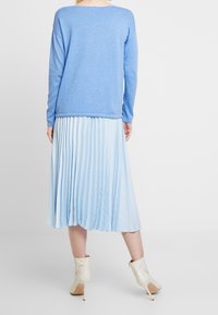 Ljusblå tröja med långa ärmar, tillsammans med en plisserad ljusblå kjol. Outfitten kompletteras med beige högklackade ankelboots.