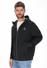 Sort lynlåstrøje med hætte, med et logo på brystet, sidelommer og elastiske manchetter, lavet af et glat, let materiale.