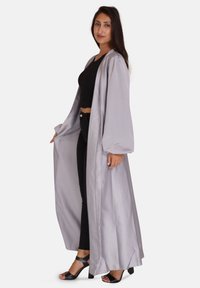Lungo kimono grigio in satin con maniche larghe, design fluido, indossato sopra un top e pantaloni neri. La modella è in tacchi su uno sfondo bianco.