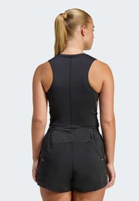 Čierne atletické tielko s priliehavým strihom a štýlom racerback, doplnené o zladené čierne šortky s vrkočovým pásom a vreckami.