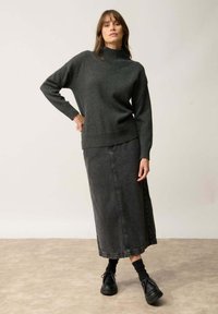 Ciemnoszary sweter robiony na drutach z wysokim kołnierzem, zestawiony z długą czarną spódnicą z denimu i czarnymi butami z wiązaniem.