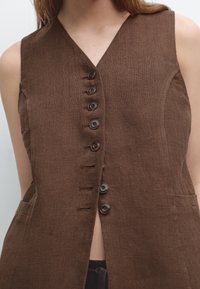 Brun linneväst utan ärmar med V-ringning, försedd med sex mörka knappar framtill och sidofickor. Texturerat tyg med en lätt vävstruktur.