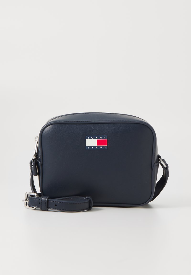 Bolsa de ombro em azul marinho, feita de material sintético liso, com um formato retangular e um logo de marca em um patch na parte da frente.