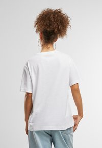 T-shirt en coton blanc à manches courtes et col rond, avec une coupe décontractée et une texture lisse. Design minimaliste sans motifs.