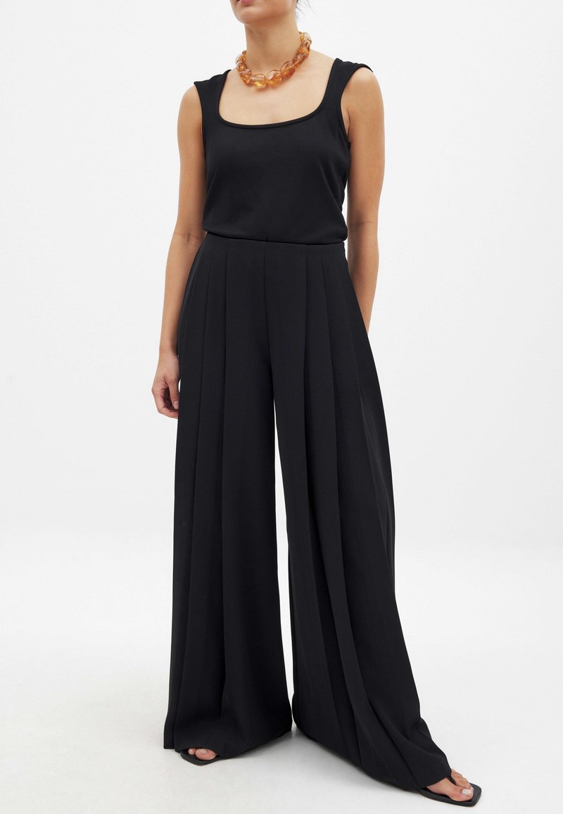 Juodas be rankovių viršus su kvadratiniu iškirpimu, derinamas su plačiomis juodomis kelnėmis, turinčiomis klostes. Modelis dėvi masyvų gintaro kaklo papuošalą.