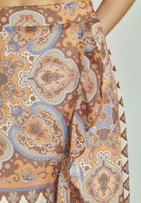 Tissu à motifs brun et orange avec des designs floraux complexes, mettant en vedette des accents bleus et une texture fluide avec des plis.