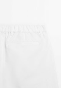 Hvide bukser med elastisk talje, der har en baglomme med en subtil sømdetalje. Glat tekstur, afslappet design.