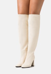 Botas de imitación de cuero blancas hasta la rodilla con punta cuadrada y tacón grueso, que presentan una textura suave y un diseño ajustado.