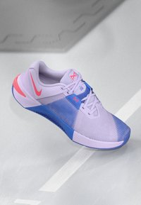 Pantoful sportiv de culoare violet, cu talpă albastră și accente roz. Dispune de un superior din plasă, un guler căptușit și un design cu șireturi pentru o fixare sigură.