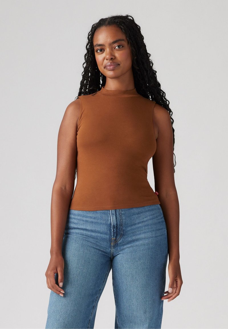 Brun uten ermer topp i en tettsittende design, laget av glatt stoff. Kombinert med lyseblå vide jeans, som viser en uformell klesstil.