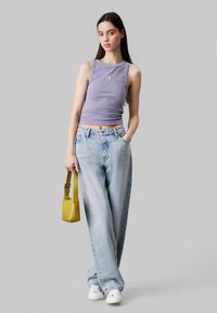 Canottiera a coste di un leggero viola con un piccolo logo dorato, jeans azzurri larghi, sneakers bianche e una piccola borsa gialla.