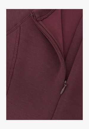 Burgunderfarbener Reißverschluss-Stoff mit glatter Textur und sichtbaren Nahtdetails. Der Reißverschluss verläuft entlang der Kante des Kleidungsstücks.