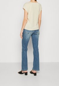 Beige kortærmet top kombineret med flagrende blå denim jeans. Jeansene har et klassisk fem-lomme design og let falmning. Sorte blokhælede sandaler.